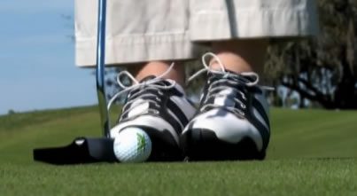 Golfer's feet, putter, and golf ball.