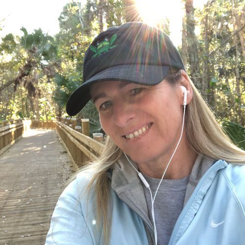 Woman smiling on boardwalk wearing frog hat.